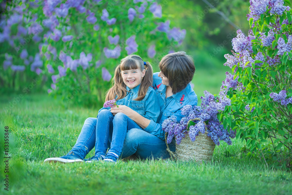 Fototapeta premium Cute adorable beautifull mother lady mom woman with brunette girl daughter in meadow of lilac purple bush.People in jeans wear.