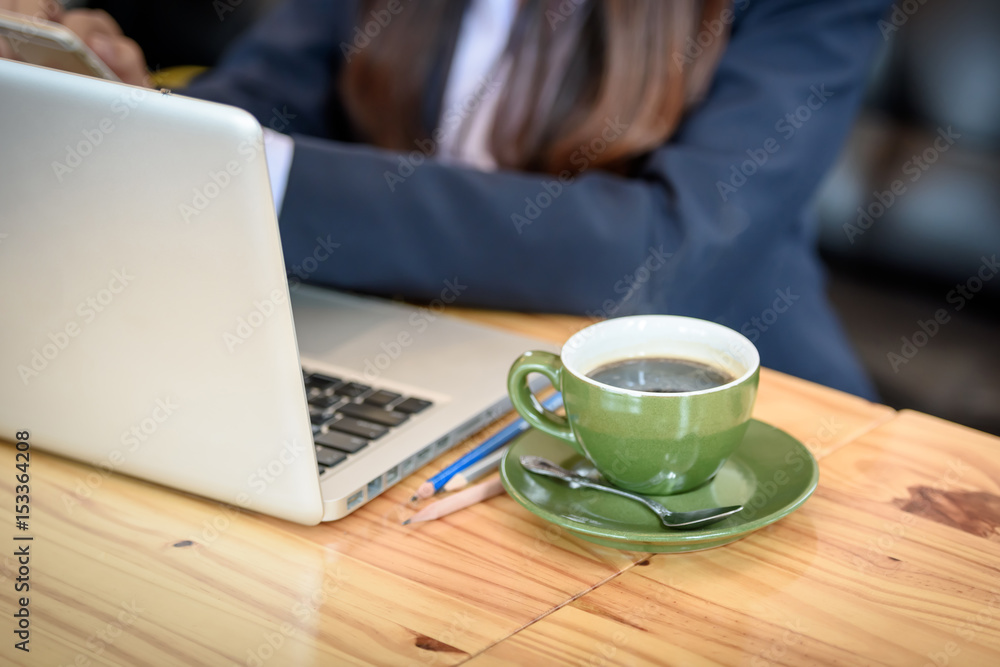 A cup of coffee is on the table beside the laptop computer. By a beautiful young businesswoman is the background. A cup of coffee is on the table beside the laptop computer. By a beautiful young businesswoman is the background.