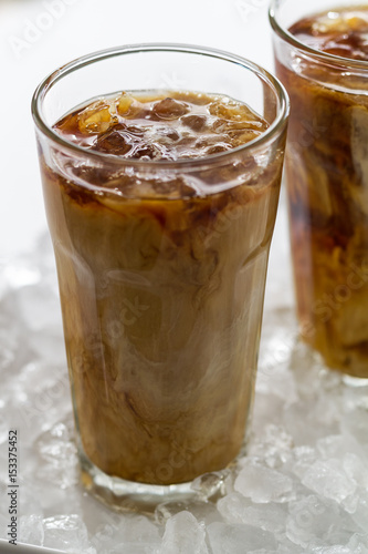 Tasty cold refreshing drink with coffee, milk and ice in glass on ice background. Closeup.