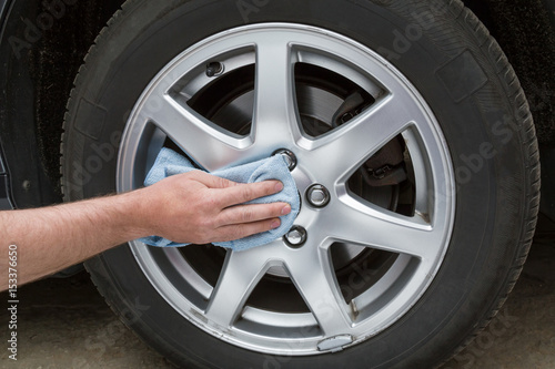 Man's hand with rag cleaning a dusty car wheel disk in the garage. Early spring washing or regular wash up. Professional car wash by hands.