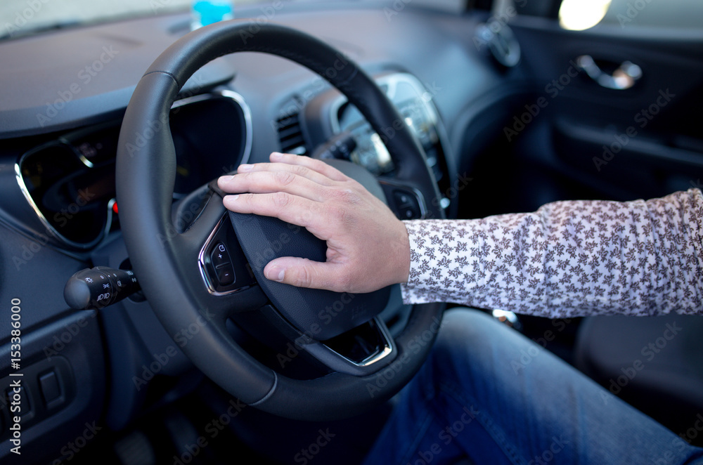The hand of a man presses on the steering wheel of a car