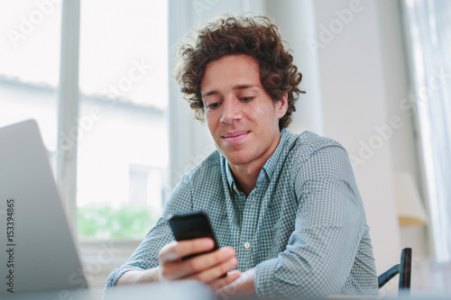 Young free lancer holding mobile phone sitting at desk photo