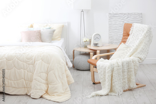 Chair near comfortable bed with soft beige coverlet and pillows in light modern room photo
