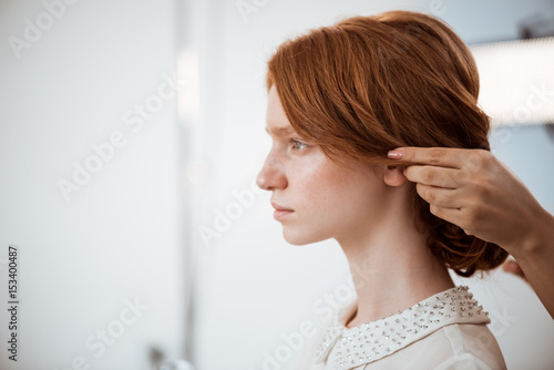 Female hairdresser making hairstyle to redhead girl in beauty salon.