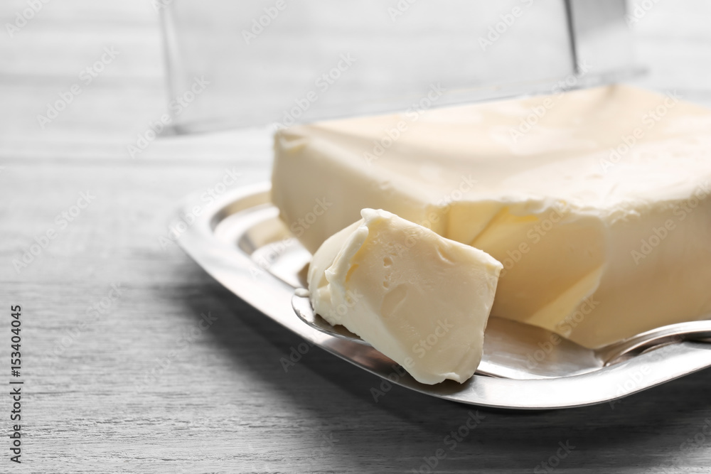 Dish with butter and shovel on wooden table, closeup
