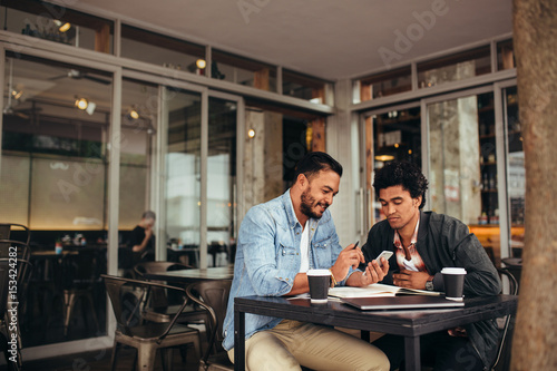 Two young men sitting at cafe using mobile phone
