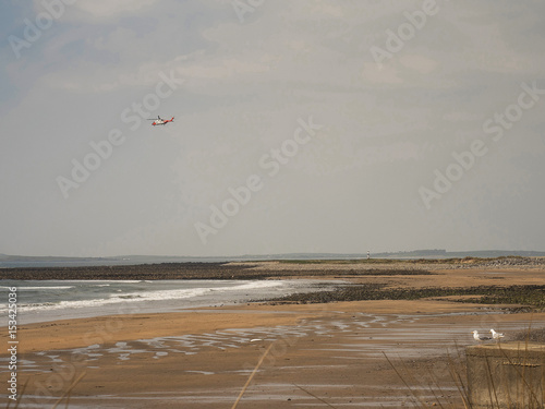 Helicopter flying over calm beach.