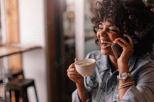 Cheerful young woman talking on phone in a cafe