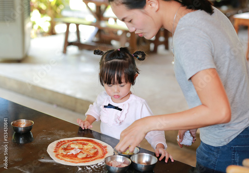 Mother and Cute little girl using Wooden rolling pin on Dough for pizza. Homemade process of preparation pizza.