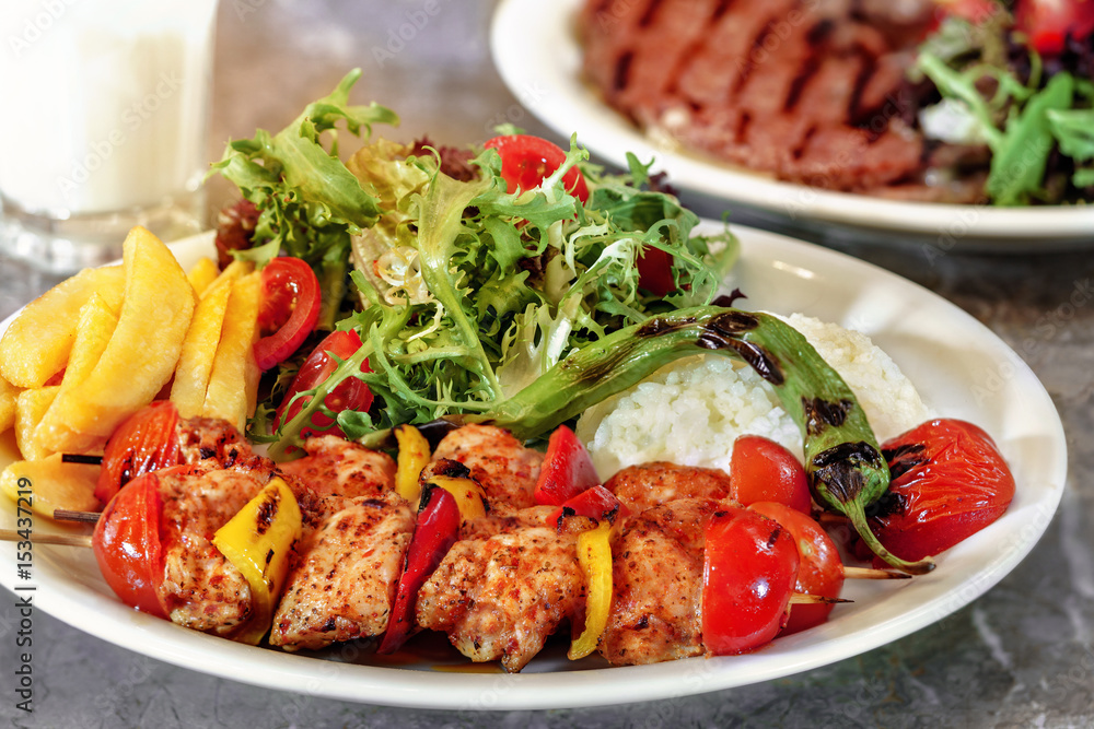 Chicken skewers, french fries and rice with leaf vegetable.