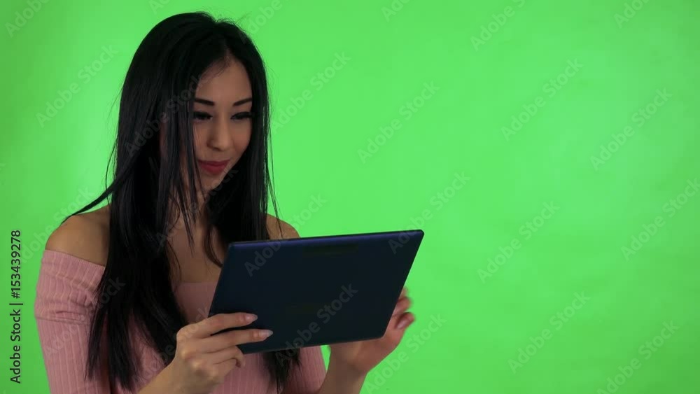 young attractive asian woman works on tablet and smiles - green screen studio