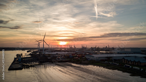 Dusk at the Port of Tilbury, Essex, UK. Sunset view of the low tide of the River Thames and wind turbines turning in the background.