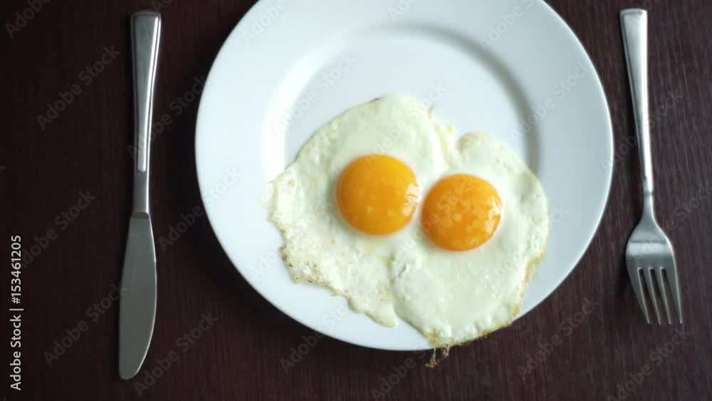 White plate with fried egg on wooden table. Serving breakfast eggs. Fried eggs on plate. Close up white porcelain plate with breakfast eggs fried. Traditional breakfast on white plate White plate with fried egg on wooden table. Serving breakfast eggs. Fried eggs on plate. Close up white porcelain plate with breakfast eggs fried. Traditional breakfast on white plate