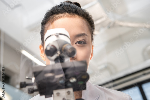 partial view of woman scientist looking through microscope on reagents in laboratory