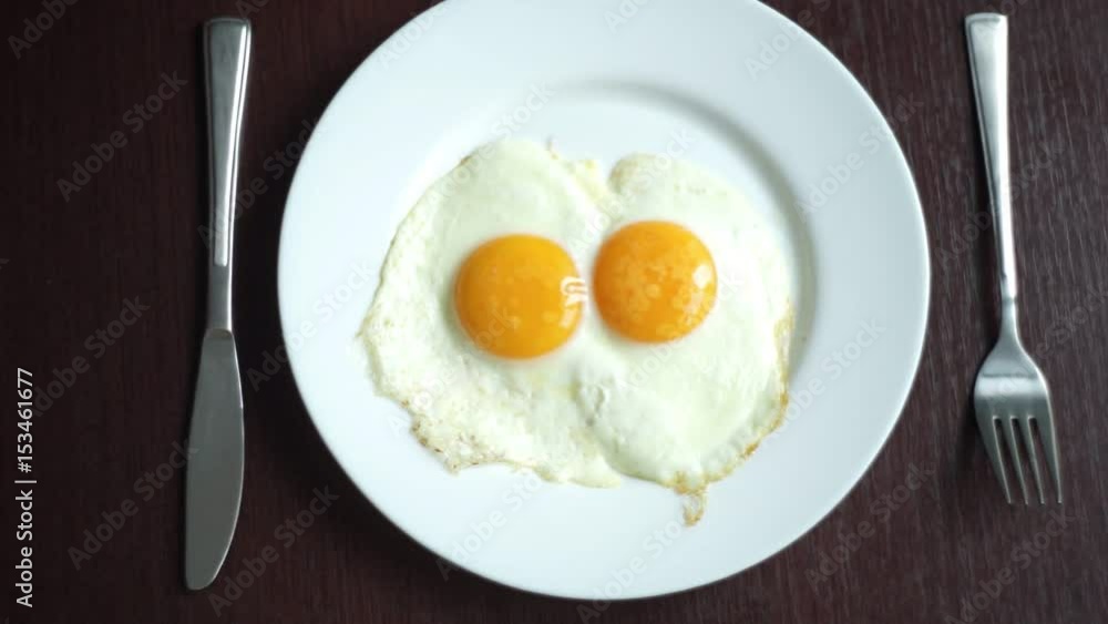 Fried eggs on plate. Putting plate with fried eggs on wooden table. Close up white porcelain plate with fried egg. Traditional breakfast meal. Serving breakfast. Breakfast food Fried eggs on plate. Putting plate with fried eggs on wooden table. Close up white porcelain plate with fried egg. Traditional breakfast meal. Serving breakfast. Breakfast food