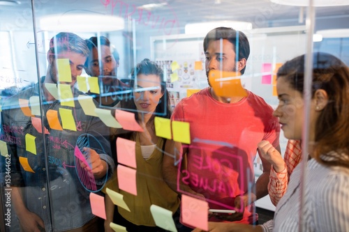 Creative business team looking at sticky notes on glass window
