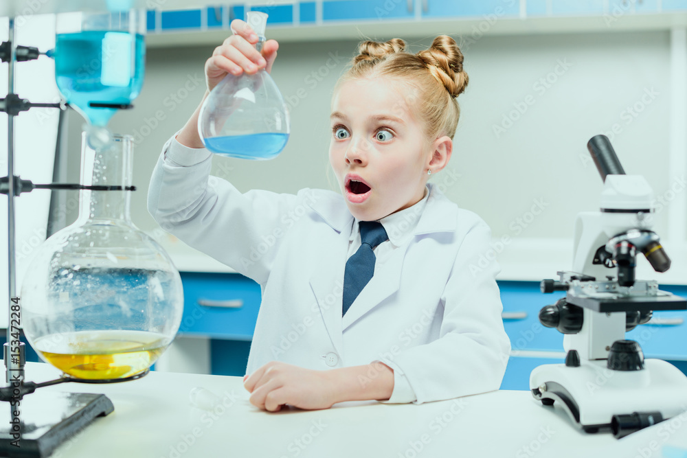 Fototapeta premium schoolgirl in white coat making experiment with reagents in chemical lab, science student concept