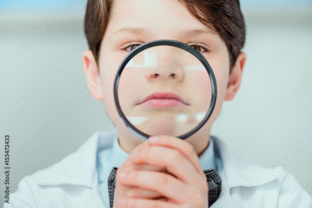 Close-up view of little scientist in white coat holding magnifier, science school concept Close-up view of little scientist in white coat holding magnifier, science school concept