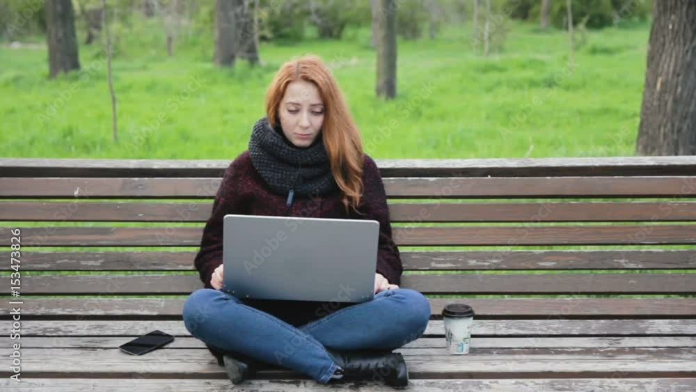 Young freelance woman in scarf having video chat using her laptop in the park Young freelance woman in scarf having video chat using her laptop in the park