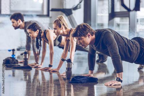 group of athletic young people in sportswear doing push ups or plank at the gym, group fitness concept
