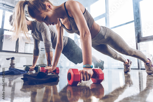 group of athletic young people in sportswear doing push ups with dumbbells at the gym, group fitness concept photo