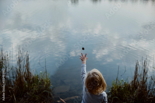 Little girl throws a pine cone into the lake