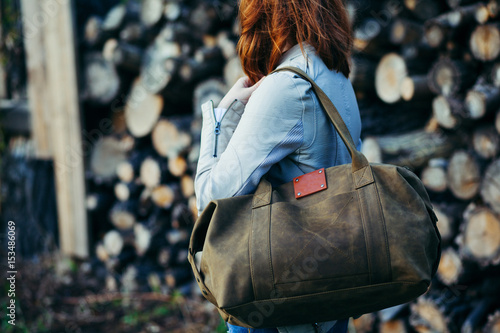 The young girl with a leather bag at a wall from logs.