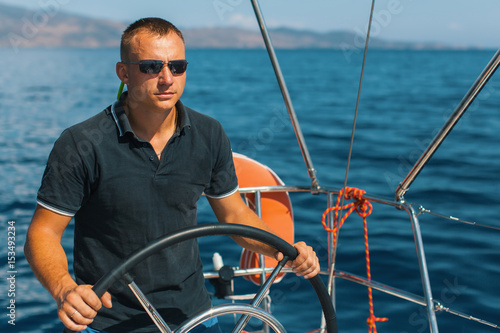 Tanned young male skipper at the helm of a sailing yacht. © De Visu