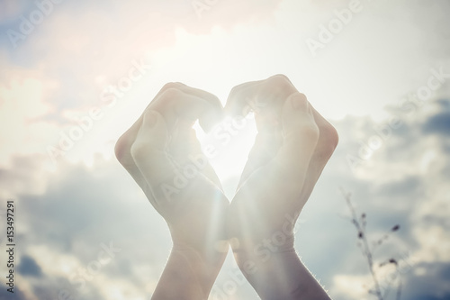 Woman making heart shape with hands against clouds