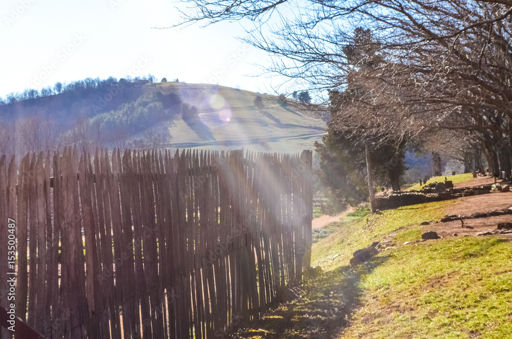 Fototapeta premium Wooden fence on farm by mountains hills in Virginia countryside with creative lens flare