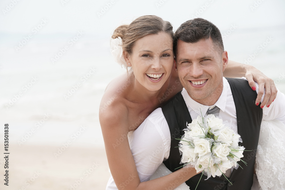 Groom giving piggyback ride to bride on the beach Groom giving piggyback ride to bride on the beach