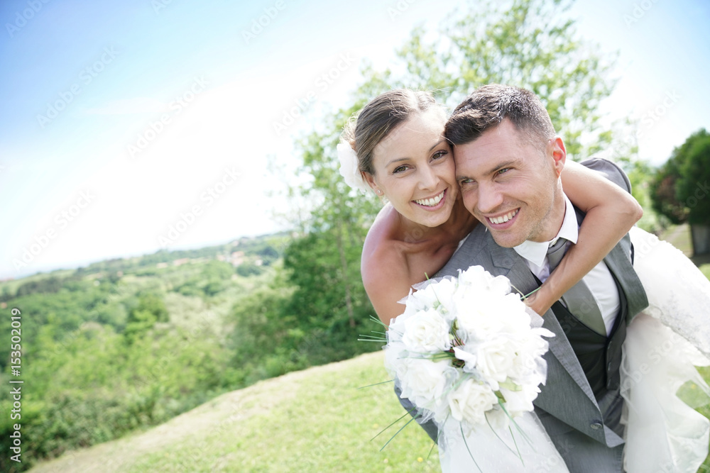 Groom giving piggyback ride to bride in countryside Groom giving piggyback ride to bride in countryside