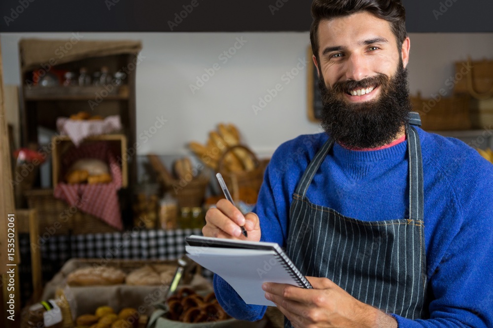 Smiling male staff writing on notepad at counter in bakery shop