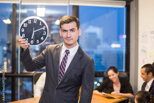 Businessman stading and holding clock with team while meeting, Businessman leader concept, 20-30 year old. photo