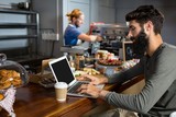 Male customer using laptop while having coffee at counter