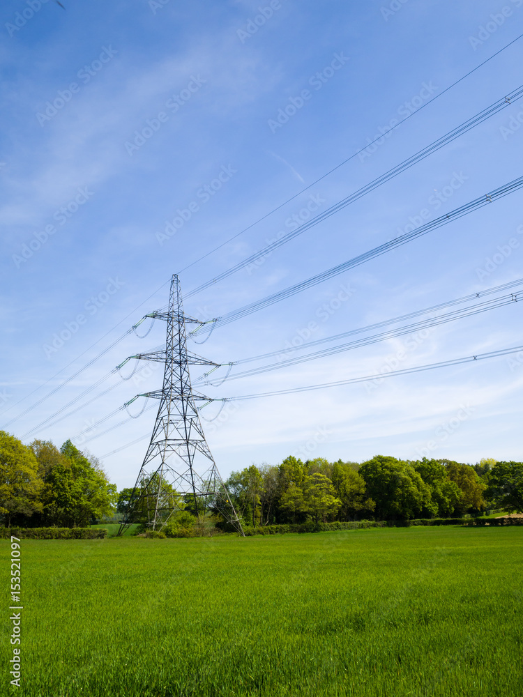 An electricity pylon in the UK with cables stretching across a farm field, against a blue sky with high cirrus clouds
