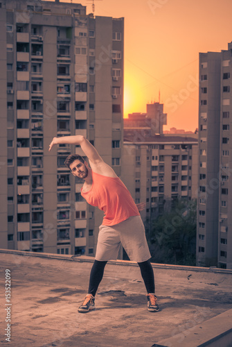 athlete stretching buildings roof rooftop, sunset sunrise Sun, warm colors