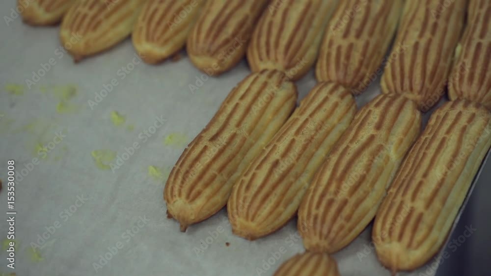 Hands of confectioner skillfully make a culinary masterpiece in candy store or pastry shop. Hands in gloves shift eclairs on steel table.Eclairs decorated with icing.Production,food industry concept. Hands of confectioner skillfully make a culinary masterpiece in candy store or pastry shop. Hands in gloves shift eclairs on steel table.Eclairs decorated with icing.Production,food industry concept.