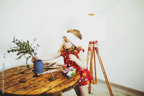 portrait of a little girl with an easel and paints, creating a painting