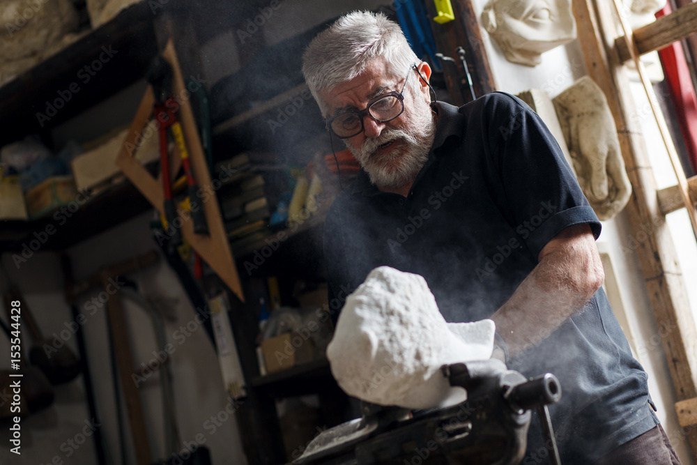 Senior sculptor working on his marble sculpture in his workshop with grinder.