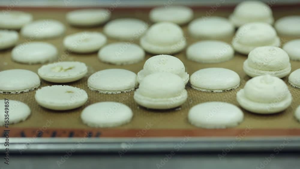 Macaroons filling and making process. Hands of chef pastry filling and laying out white macaroons on steel table which is laid out with baking paper. Food industry, mass or volume production. Macaroons filling and making process. Hands of chef pastry filling and laying out white macaroons on steel table which is laid out with baking paper. Food industry, mass or volume production.