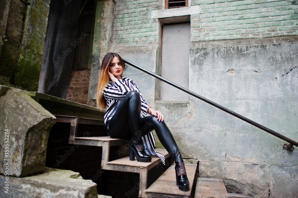 Fashionable woman look with black and white striped suit jacket, leather pants, posing at old street on iron stairs. Concept of fashion girl. Fashionable woman look with black and white striped suit jacket, leather pants, posing at old street on iron stairs. Concept of fashion girl.