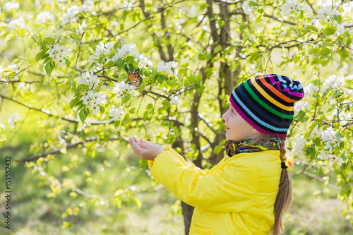 Cute little girl is catching a butterfly in the park. Around the blossoming apple-tree. Blossoming apple-tree background.