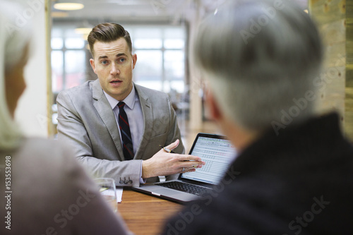 Businessman explaining to colleagues over laptop in office meeting