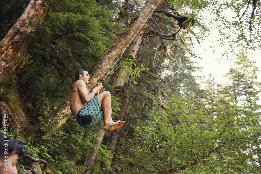 Low angle view of man swinging on rope in forest Low angle view of man swinging on rope in forest