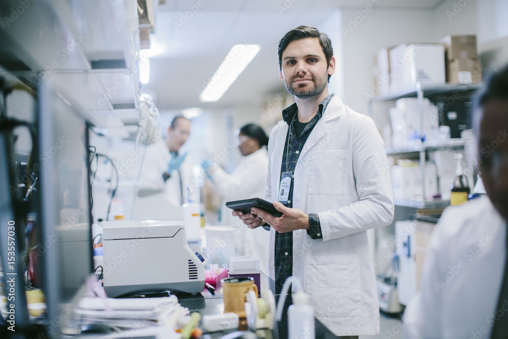 Portrait of male doctor with tablet computer and coworkers working in medical room