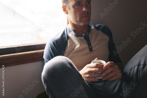 Thoughtful man with coffee cup sitting by window at home