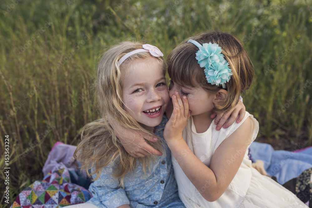 Girl whispering in sister's ear while sitting in park Girl whispering in sister's ear while sitting in park