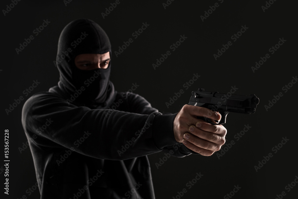 The robber in a mask with a gun pointed to the side on a black background The robber in a mask with a gun pointed to the side on a black background