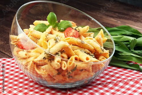 Penne pasta in tomato sauce with chicken, tomatoes decorated with basil on a wooden table